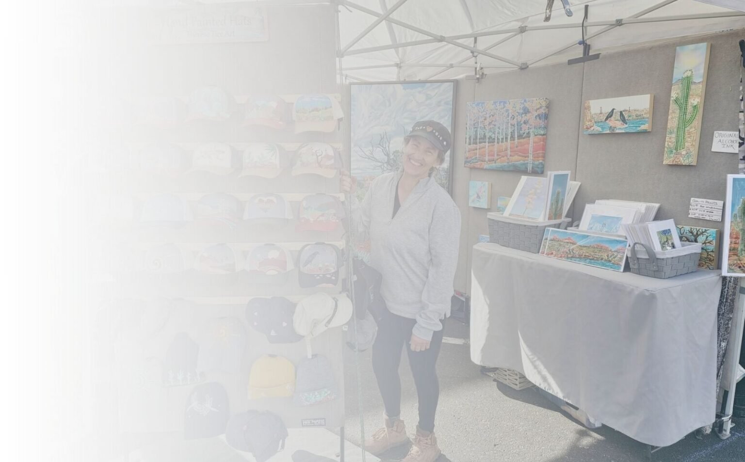 Maui artist Therese Tice standing at her art booth displaying hand-painted hats and original artwork.